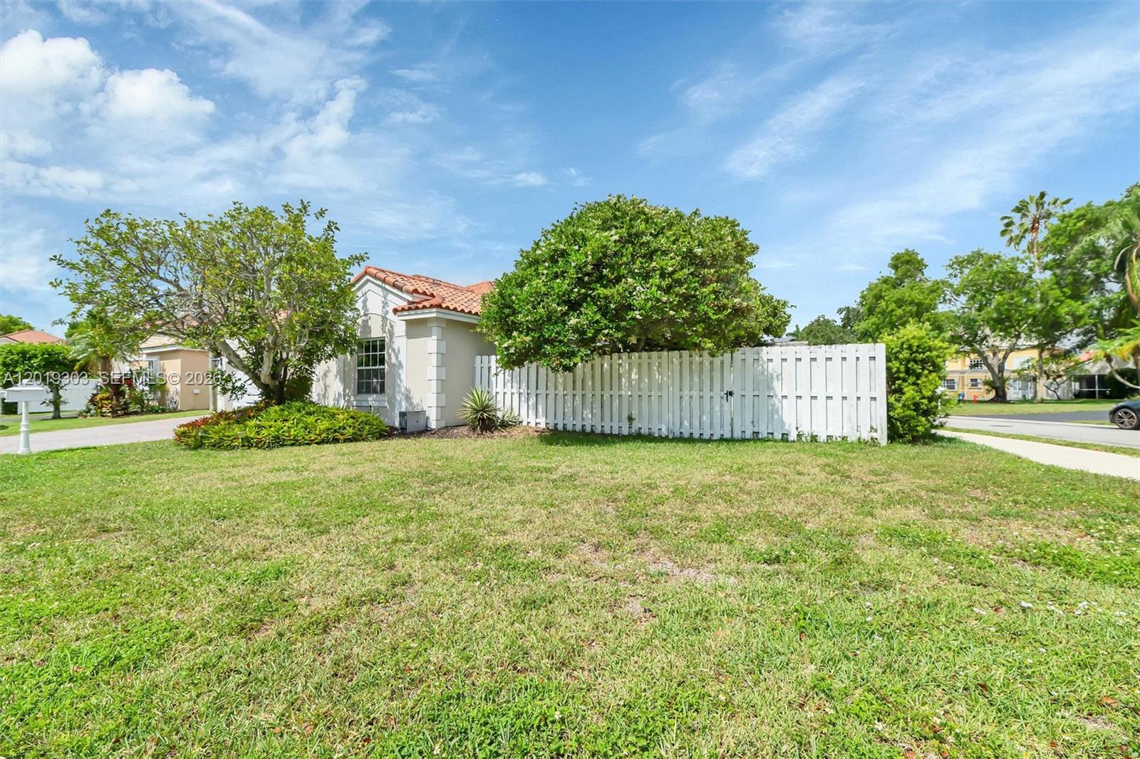 A single-story house with a white picket fence and a tiled roof sits on a lawn — 535 Somerset Way, Weston FL 33326, WESTON, FL