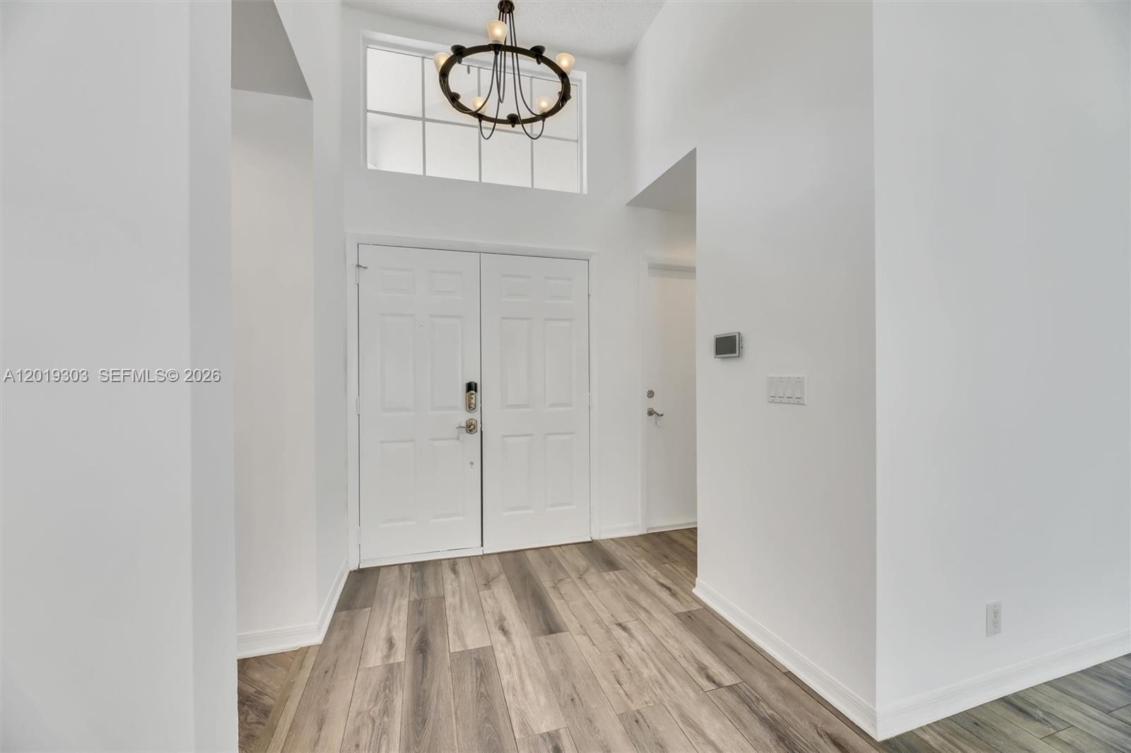 A bright entryway features white walls, wood-look flooring, a double front door, and a chandelier — 535 Somerset Way, Weston FL 33326, WESTON, FL