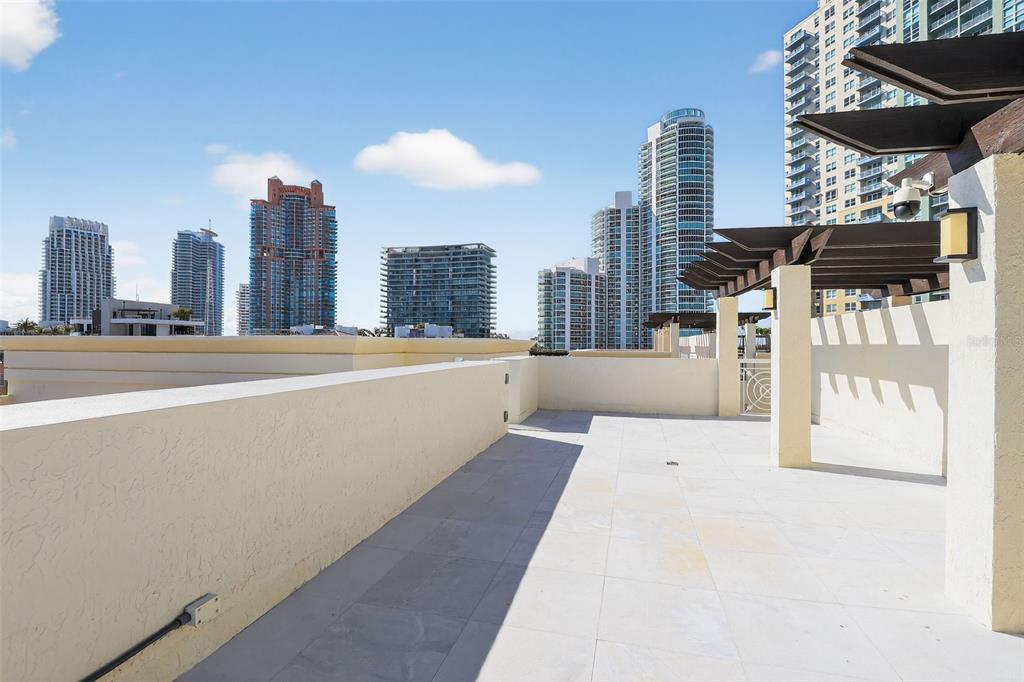 A spacious rooftop terrace features light-colored tile flooring and a pergola overlooking city skyscrapers — 120 JEFFERSON AVENUE UNIT 12009, MIAMI BEACH, FL