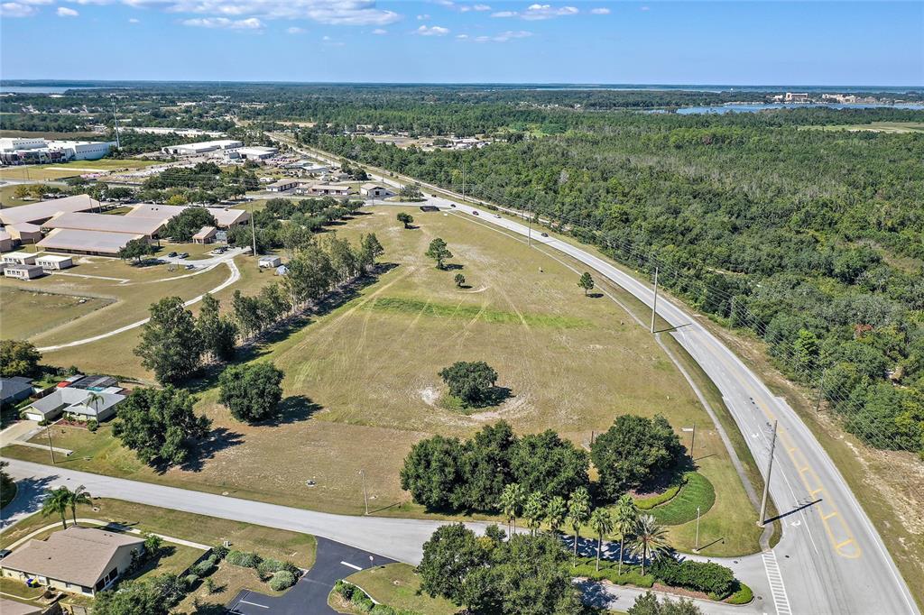 An aerial view shows a large, undeveloped grassy lot bordering a road and wooded area — CR 561 & LANE PARK CUTOFF, TAVARES, FL