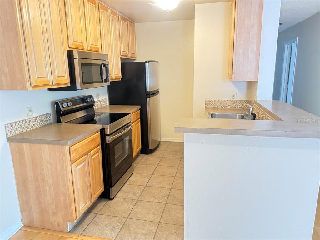 A kitchen features light wood cabinets, stainless steel appliances, and a tiled floor — 6088 WESTGATE DRIVE UNIT 203, ORLANDO, FL