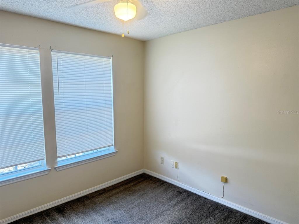 An empty bedroom features beige walls, dark carpeting, two windows with blinds, and a ceiling fan — 6088 WESTGATE DRIVE UNIT 203, ORLANDO, FL