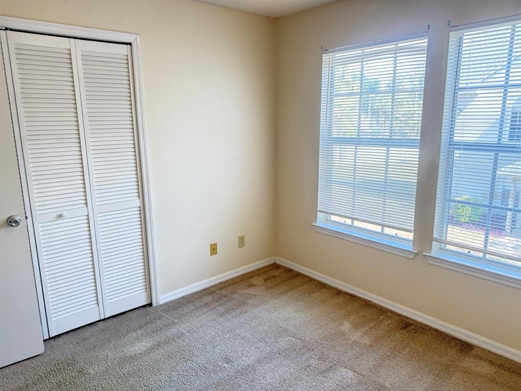 An empty bedroom features beige walls, brown carpeting, a white louvered closet, and two windows — 6088 WESTGATE DRIVE UNIT 203, ORLANDO, FL