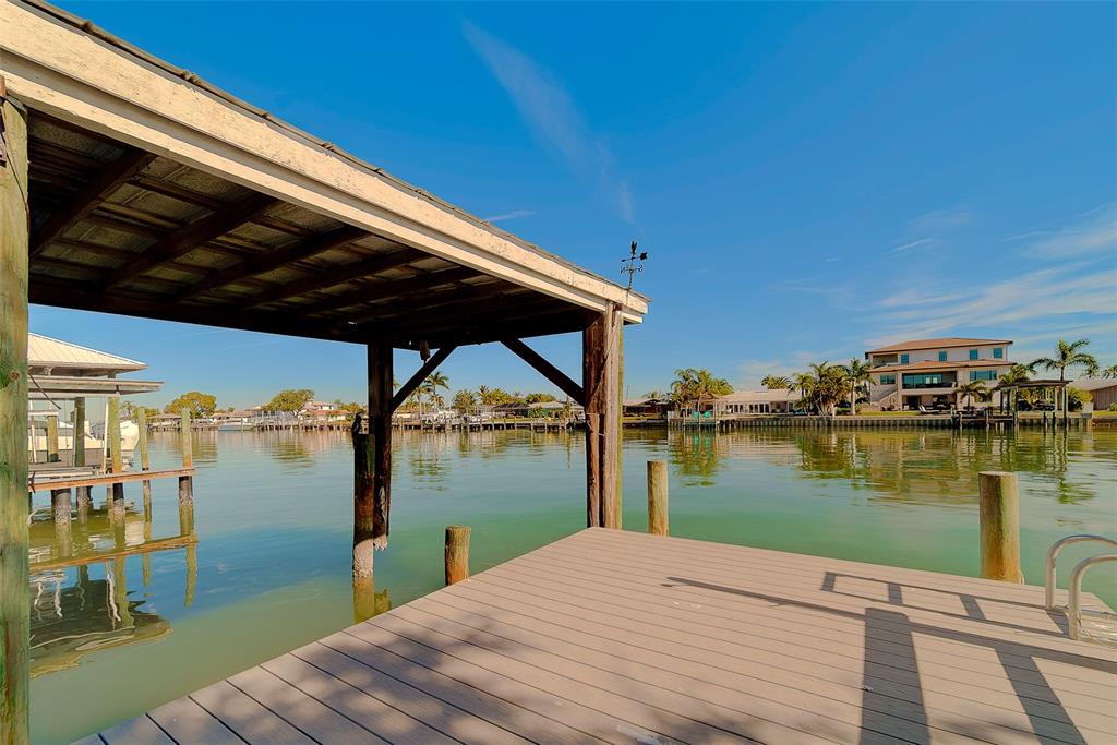 A wooden boat dock with a covered slip overlooks a calm canal and waterfront homes — 207 MIDWAY ISLAND, CLEARWATER BEACH, FL