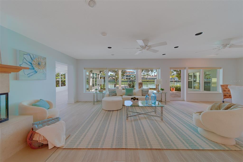 A bright living room features a white sectional, two armchairs, and large windows overlooking water — 207 MIDWAY ISLAND, CLEARWATER BEACH, FL