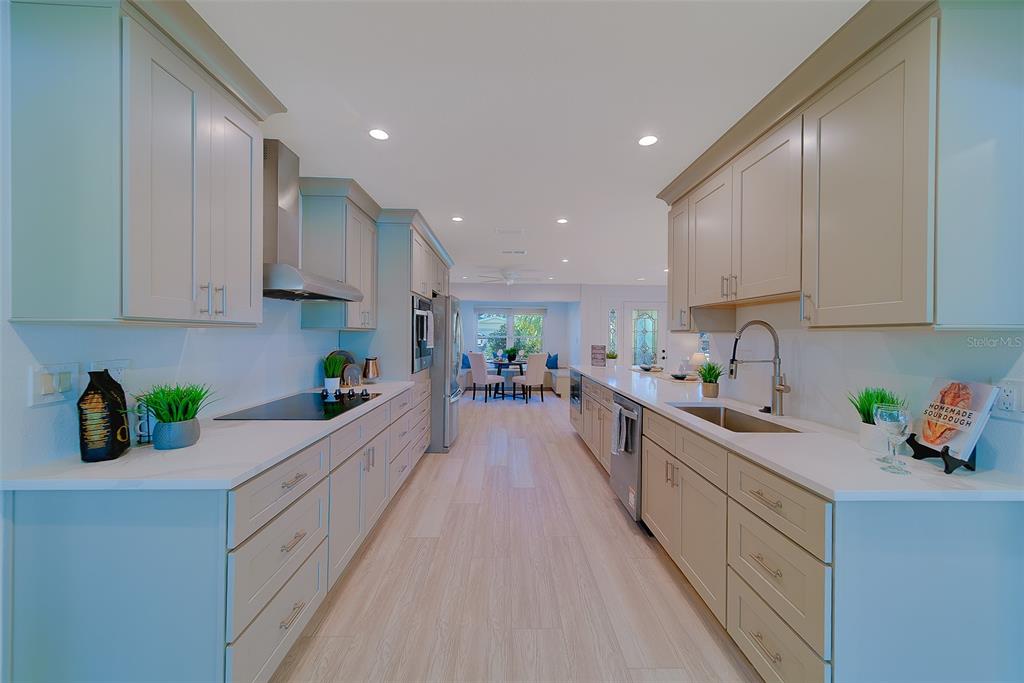 A galley kitchen features light-colored cabinetry, white countertops, stainless steel appliances, and wood-look flooring — 207 MIDWAY ISLAND, CLEARWATER BEACH, FL
