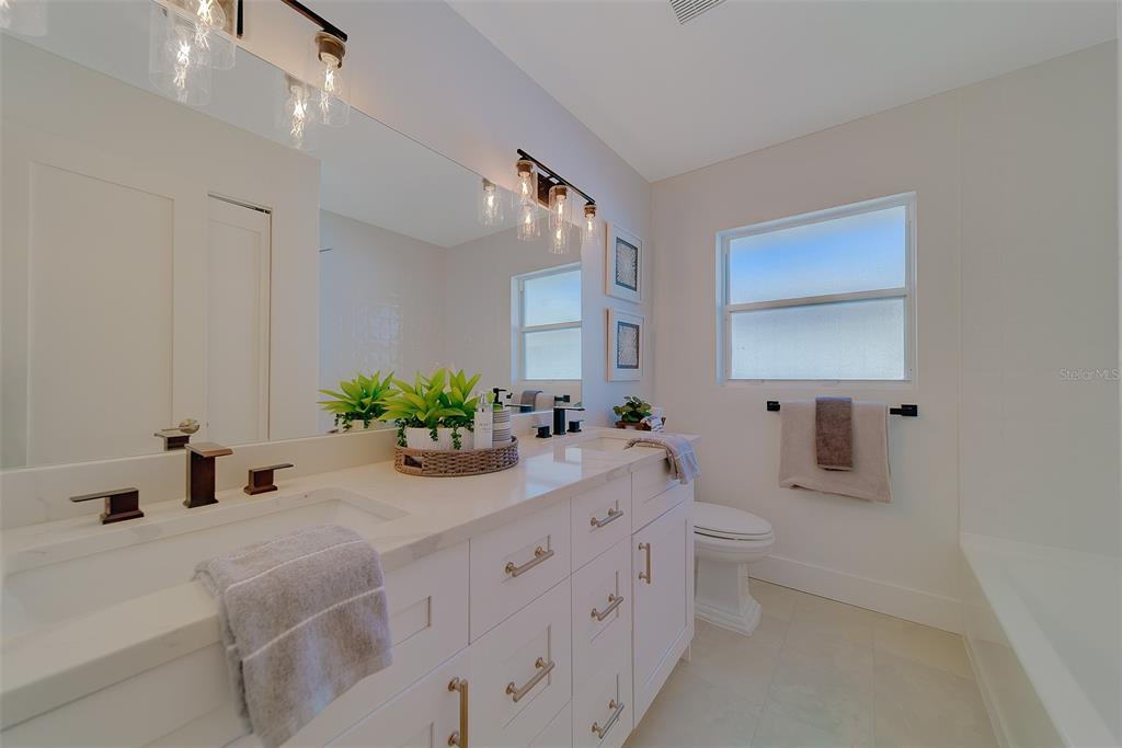 A bright bathroom features a white double vanity with gold hardware and a large mirror — 207 MIDWAY ISLAND, CLEARWATER BEACH, FL