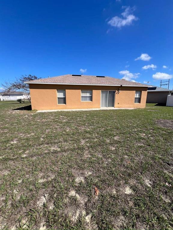 The exterior rear view of a single-story tan house with a shingled roof and yard — 735 COLVILLE PLACE, KISSIMMEE, FL