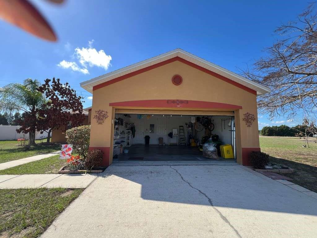 A detached garage with a tan stucco exterior and red trim sits behind a concrete driveway — 735 COLVILLE PLACE, KISSIMMEE, FL