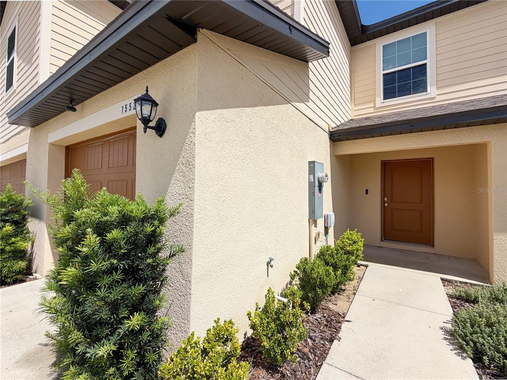 A beige two-story townhouse exterior features a brown garage door, front door, and landscaping — 1552 WYNFORD CIRCLE, TAVARES, FL
