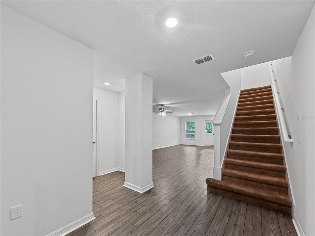 An interior view shows a carpeted staircase next to an open living area with wood flooring — 1552 WYNFORD CIRCLE, TAVARES, FL