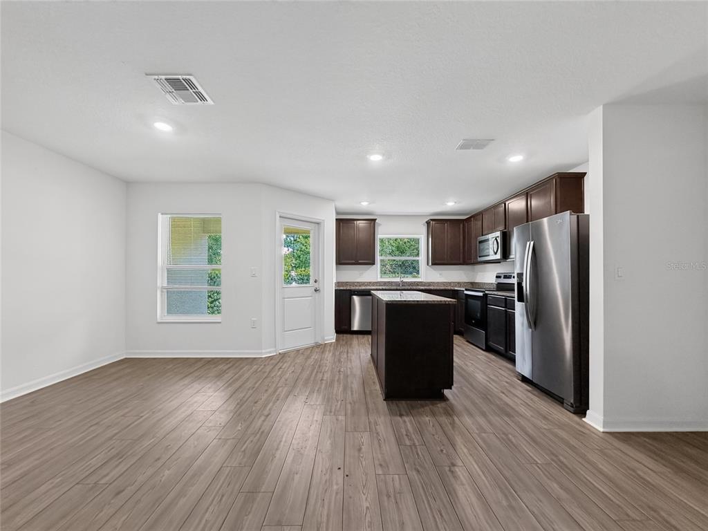 A kitchen with dark wood cabinets, stainless steel appliances, an island, and wood-look flooring — 1552 WYNFORD CIRCLE, TAVARES, FL