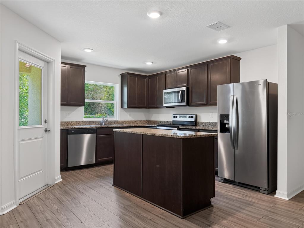 A kitchen features dark wood cabinets, granite countertops, stainless steel appliances, and a central island — 1552 WYNFORD CIRCLE, TAVARES, FL