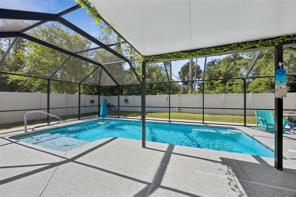 A screened-in swimming pool with a concrete deck and a white vinyl privacy fence — 1 BRUNSWICK LANE, PALM COAST, FL