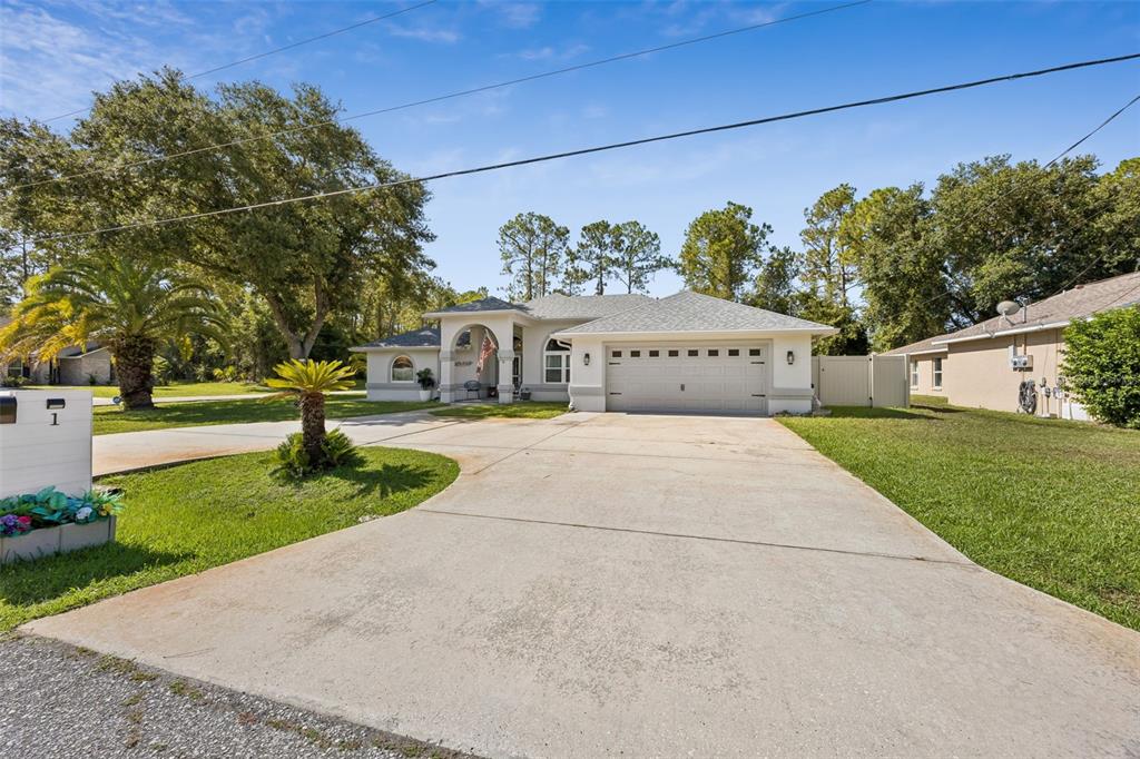A single-story house with a two-car garage and a concrete driveway sits on a lawn — 1 BRUNSWICK LANE, PALM COAST, FL