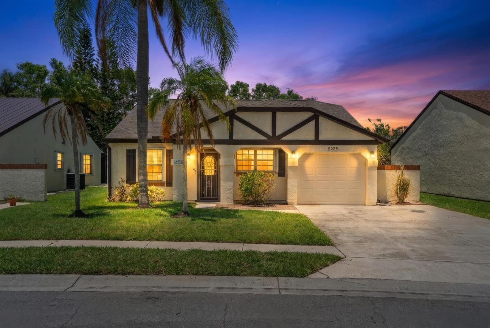 A single-story house with a garage, stucco exterior, and palm trees at dusk — 2225 SE Barrington Street, FL 34952, FL