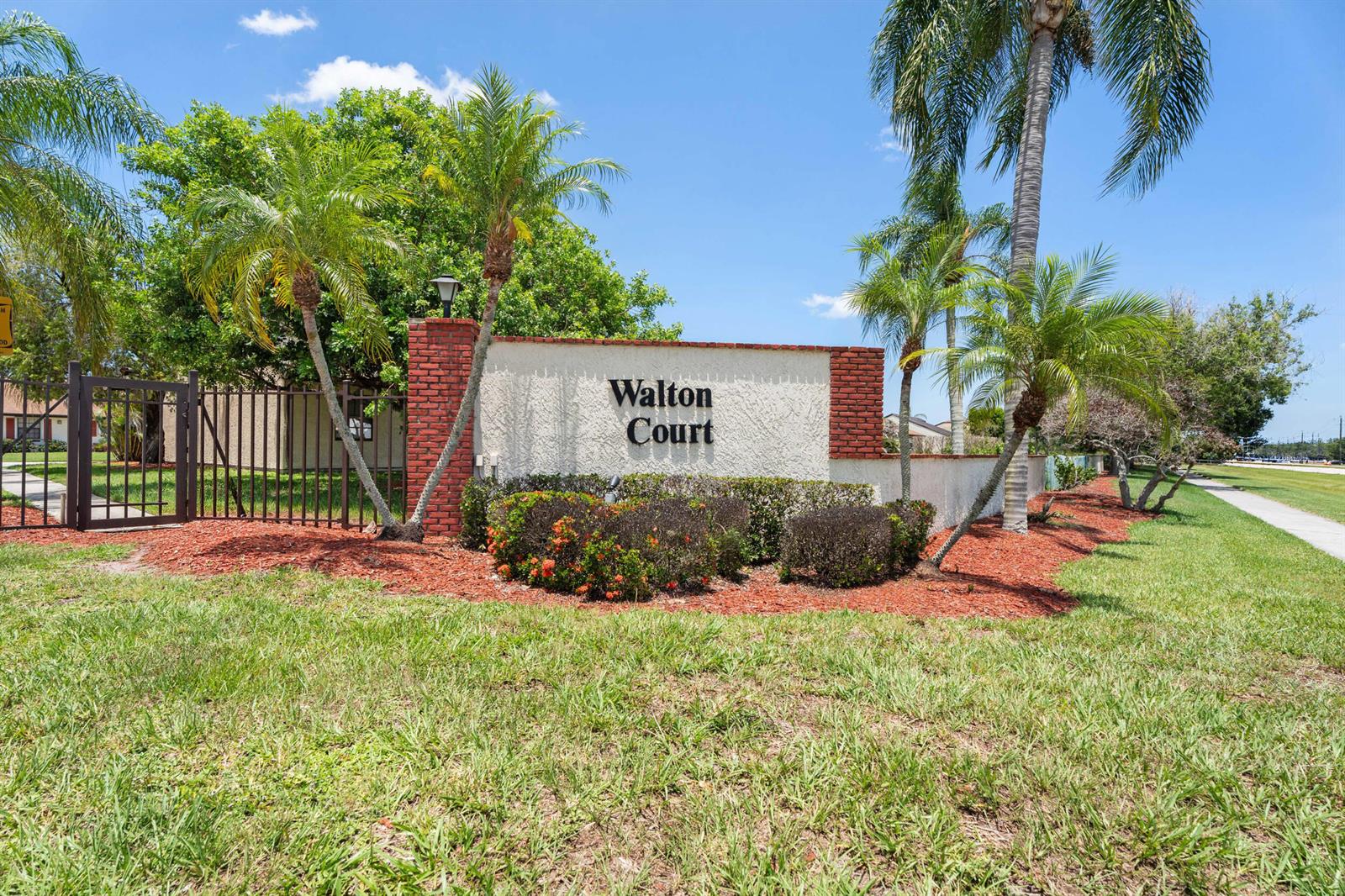 A white stucco sign with brick accents reads Walton Court in front of palm trees — 2225 SE Barrington Street, FL 34952, FL