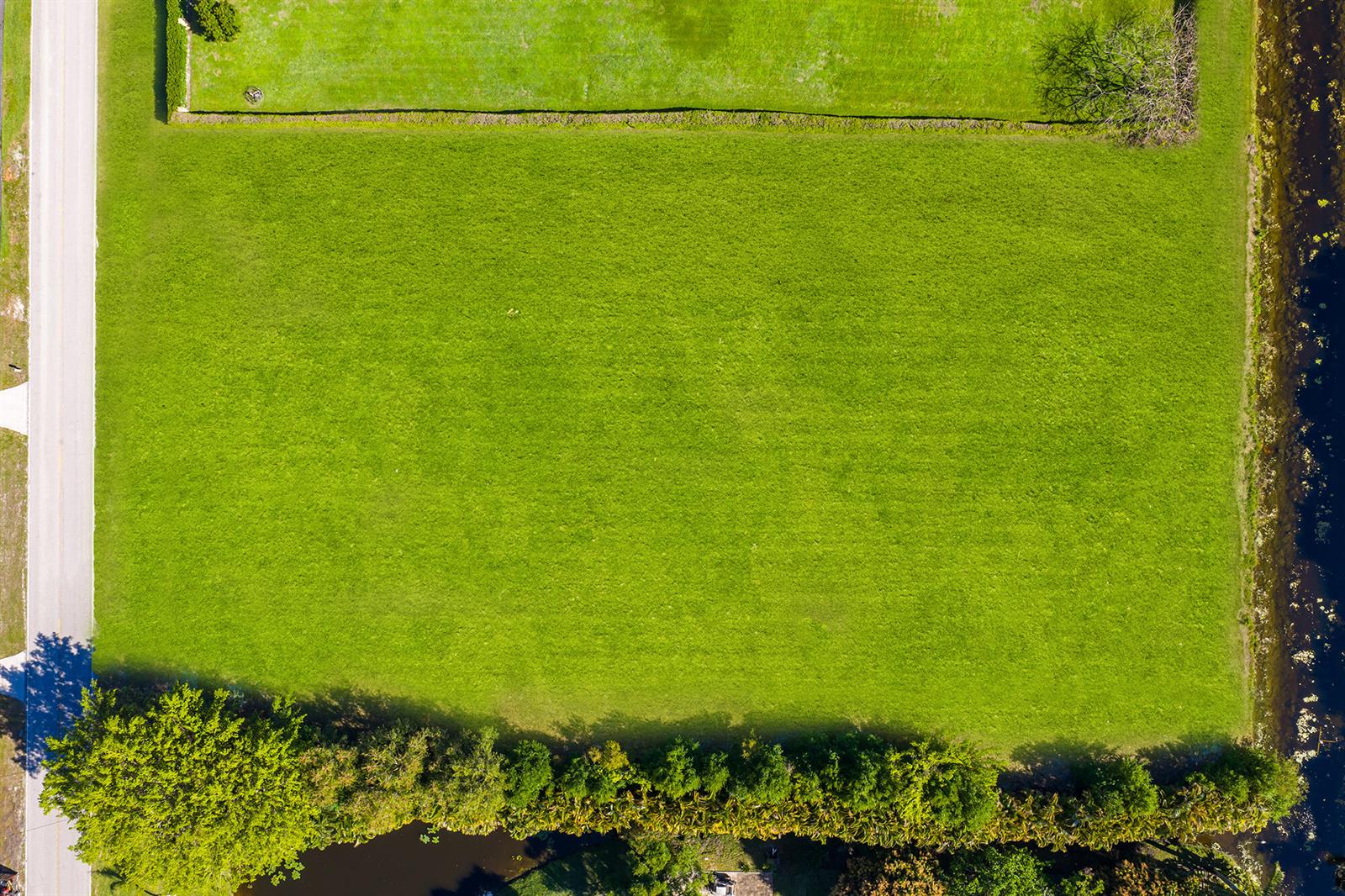 An aerial view shows a rectangular, grassy vacant lot bordered by a road and water — 14404 Wellington Trace, Wellington FL 33414, WELLINGTON, FL