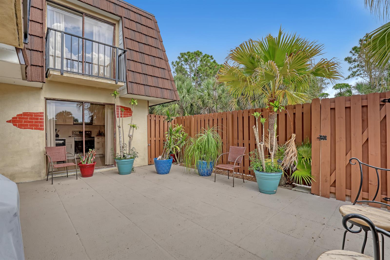 A concrete patio features potted plants, two chairs, and a wooden fence against a building — 5808 SE Riverboat Drive # 304, Stuart FL 34997, STUART, FL