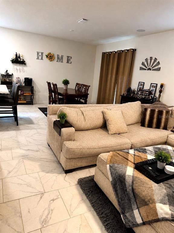 A living room features a beige sofa, a plaid ottoman, and a dining area nearby — 2726 89TH STREET CIRCLE E, PALMETTO, FL