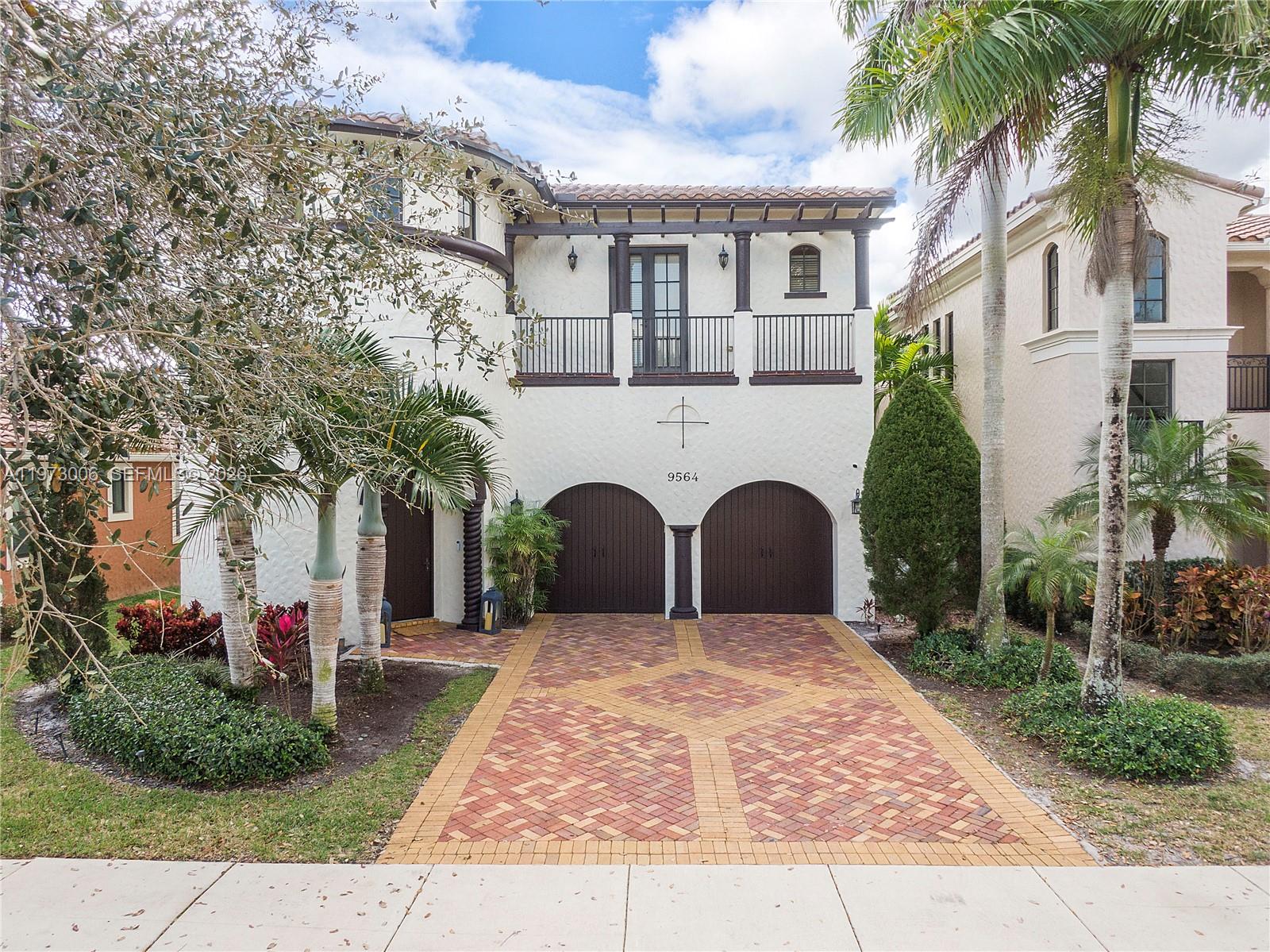 A two-story Mediterranean-style house features a brick driveway, arched garage doors, and a balcony — 9564 Exbury Ct, Parkland FL 33076, PARKLAND, FL