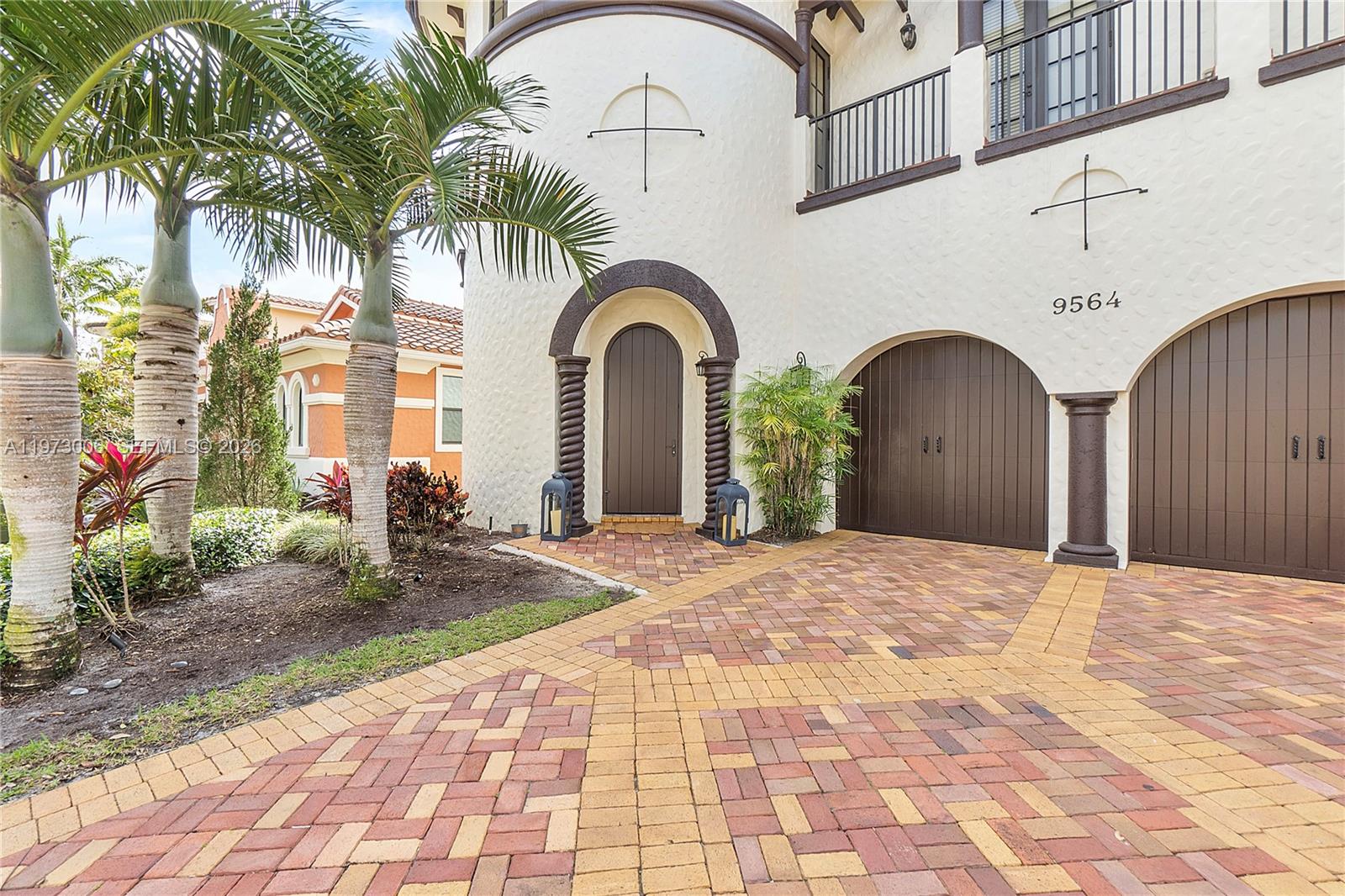 A Mediterranean-style home exterior features a brick driveway, arched garage doors, and palm trees — 9564 Exbury Ct, Parkland FL 33076, PARKLAND, FL