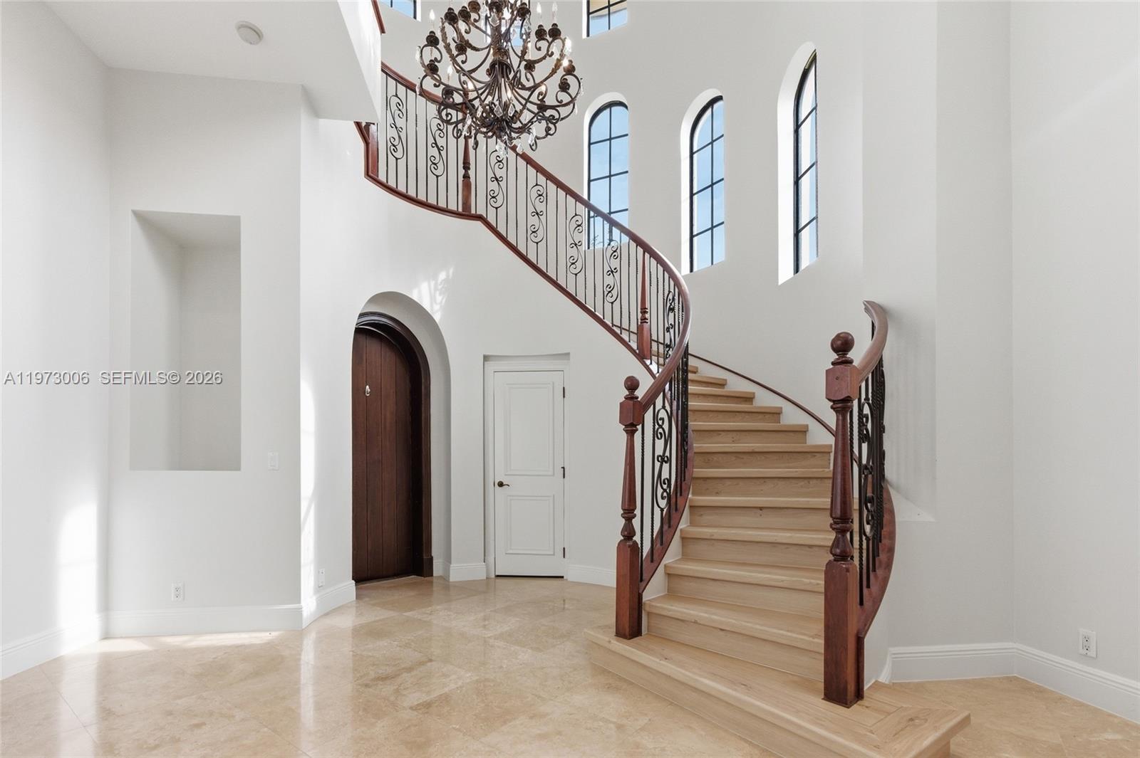 A grand foyer features a curved wooden staircase with iron railings and a large chandelier — 9564 Exbury Ct, Parkland FL 33076, PARKLAND, FL