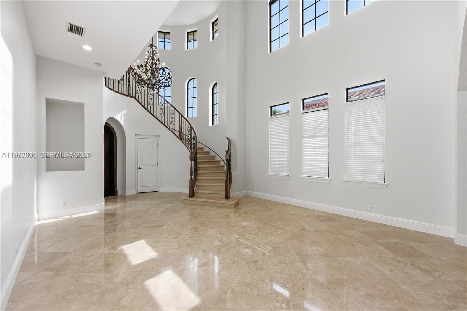 A grand foyer features a curved staircase, a chandelier, and polished stone flooring — 9564 Exbury Ct, Parkland FL 33076, PARKLAND, FL