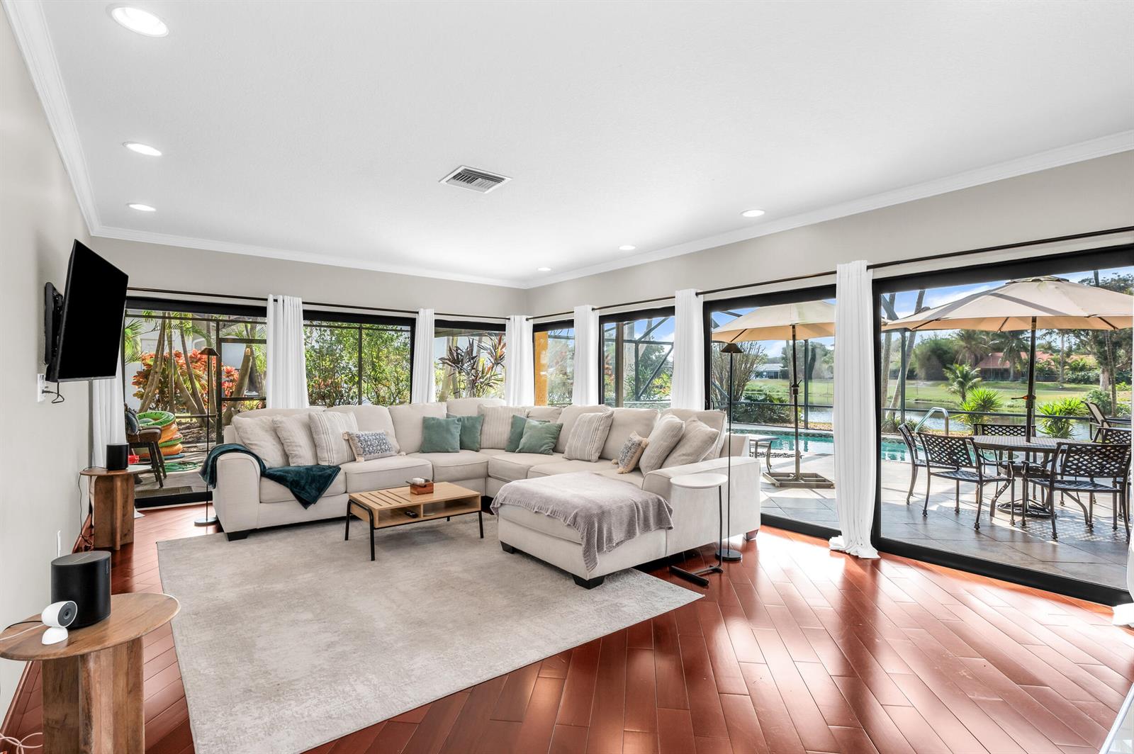 A living room features a large sectional sofa, hardwood floors, and sliding glass doors to a pool — 3250 Lakeview Boulevard, Delray Beach FL 33445, DELRAY BEACH, FL