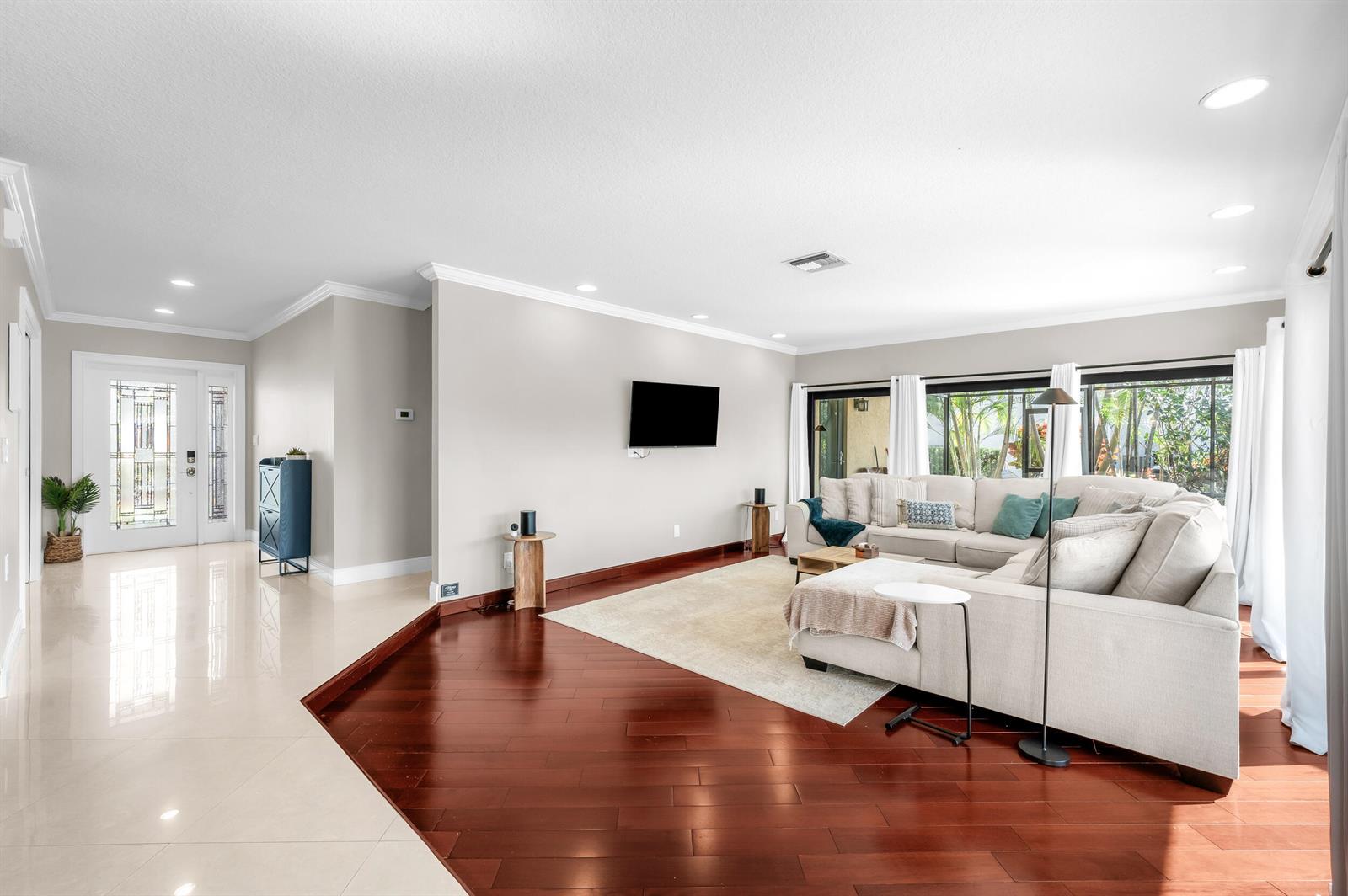 A living room features hardwood floors, a large sectional sofa, and a wall-mounted television — 3250 Lakeview Boulevard, Delray Beach FL 33445, DELRAY BEACH, FL
