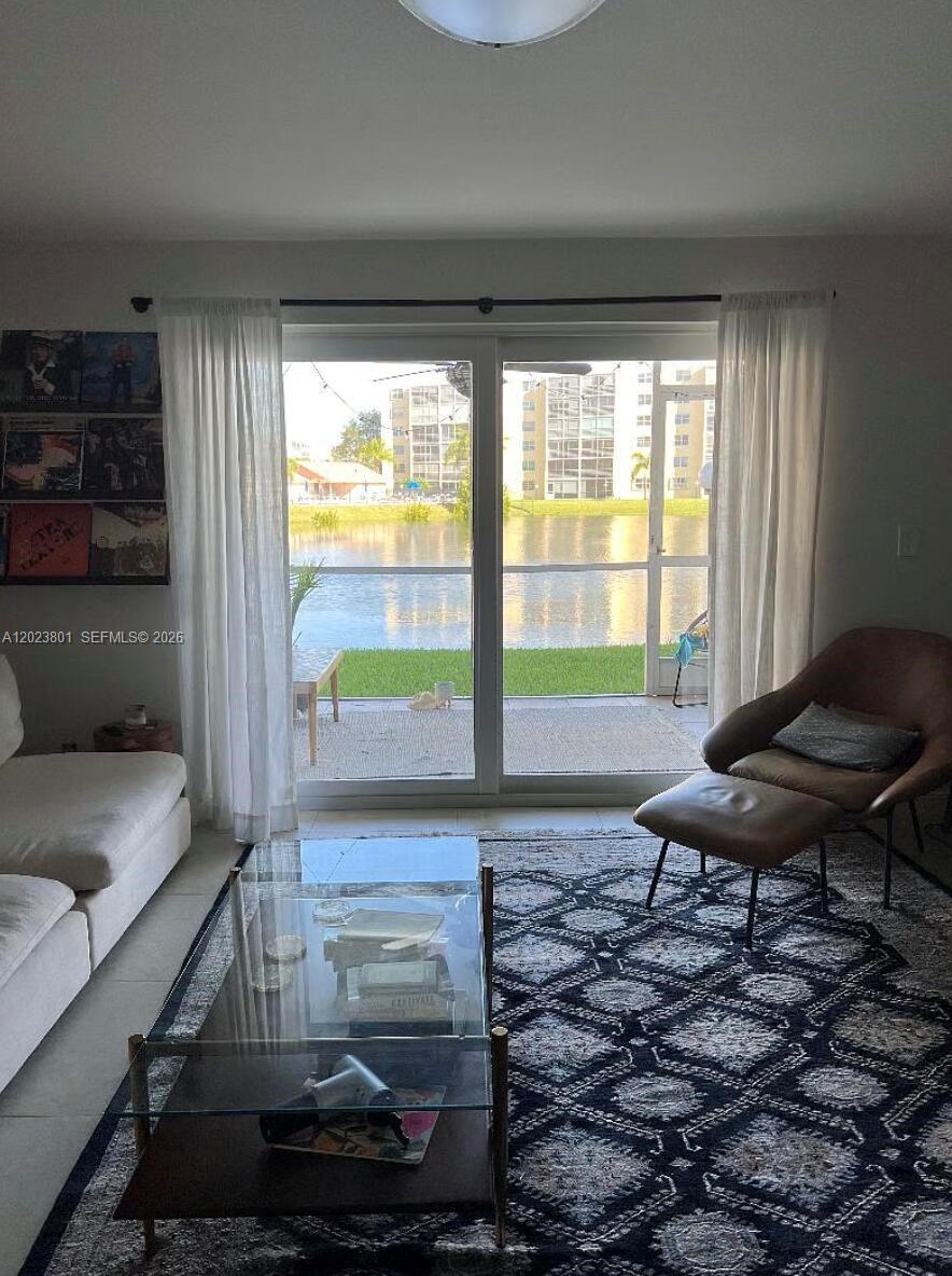 A living room features a glass coffee table, a brown armchair, and sliding doors overlooking a lake — 441 SE 3rd St # 104, Dania Beach FL 33004, DANIA BEACH, FL