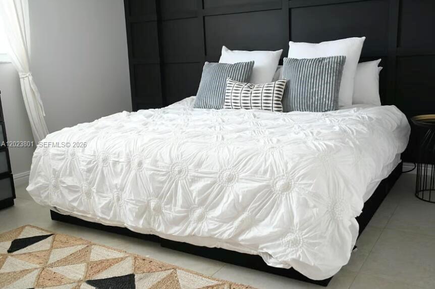 A bedroom features a white tufted comforter, gray accent pillows, and a black paneled wall — 441 SE 3rd St # 104, Dania Beach FL 33004, DANIA BEACH, FL