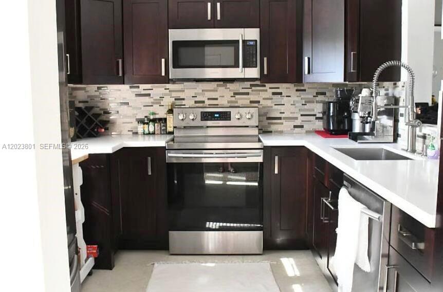 A kitchen features dark wood cabinets, stainless steel appliances, and a tiled backsplash — 441 SE 3rd St # 104, Dania Beach FL 33004, DANIA BEACH, FL