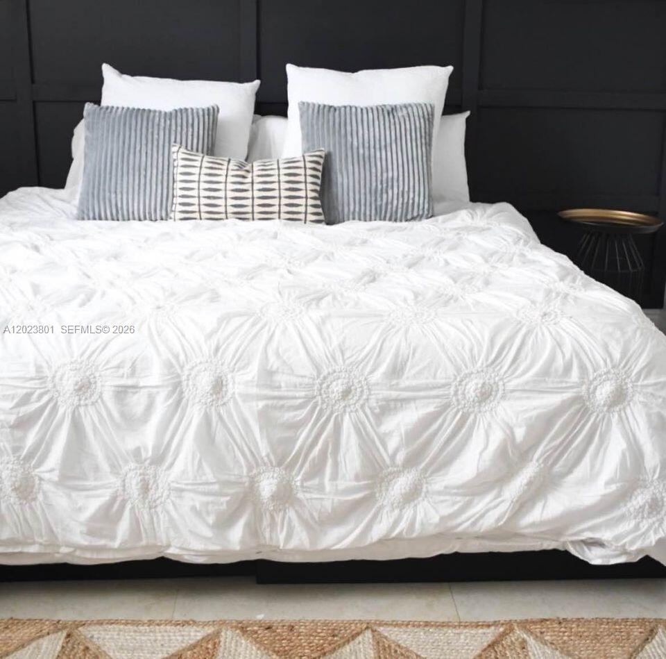 A bed with white textured bedding and decorative pillows sits against a black paneled wall — 441 SE 3rd St # 104, Dania Beach FL 33004, DANIA BEACH, FL