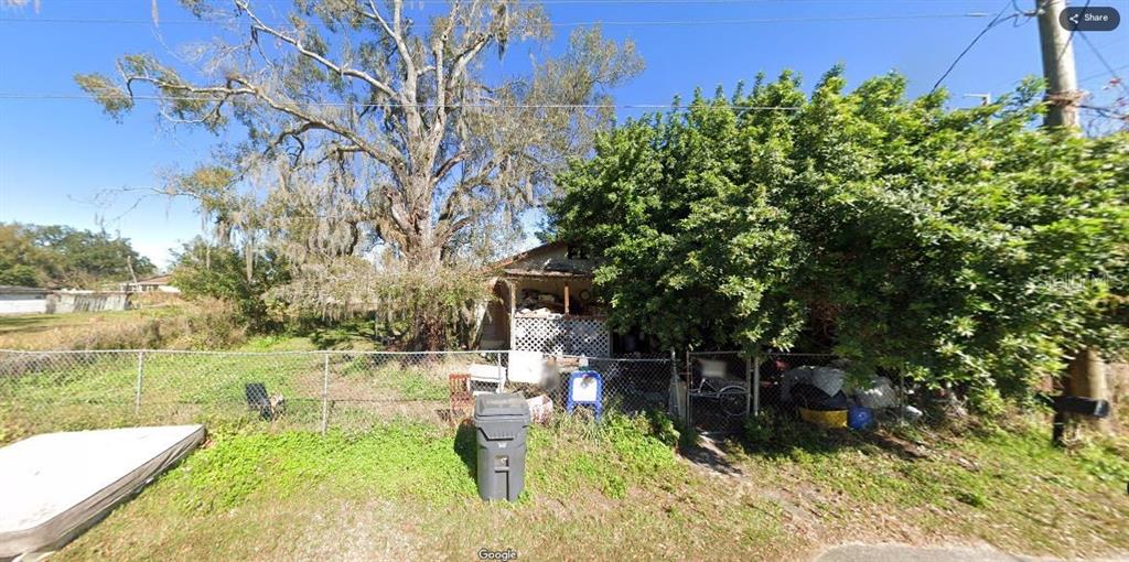 A small, weathered house sits behind a chain-link fence beneath a large, moss-covered tree — 2528 WEBER STREET, LAKELAND, FL