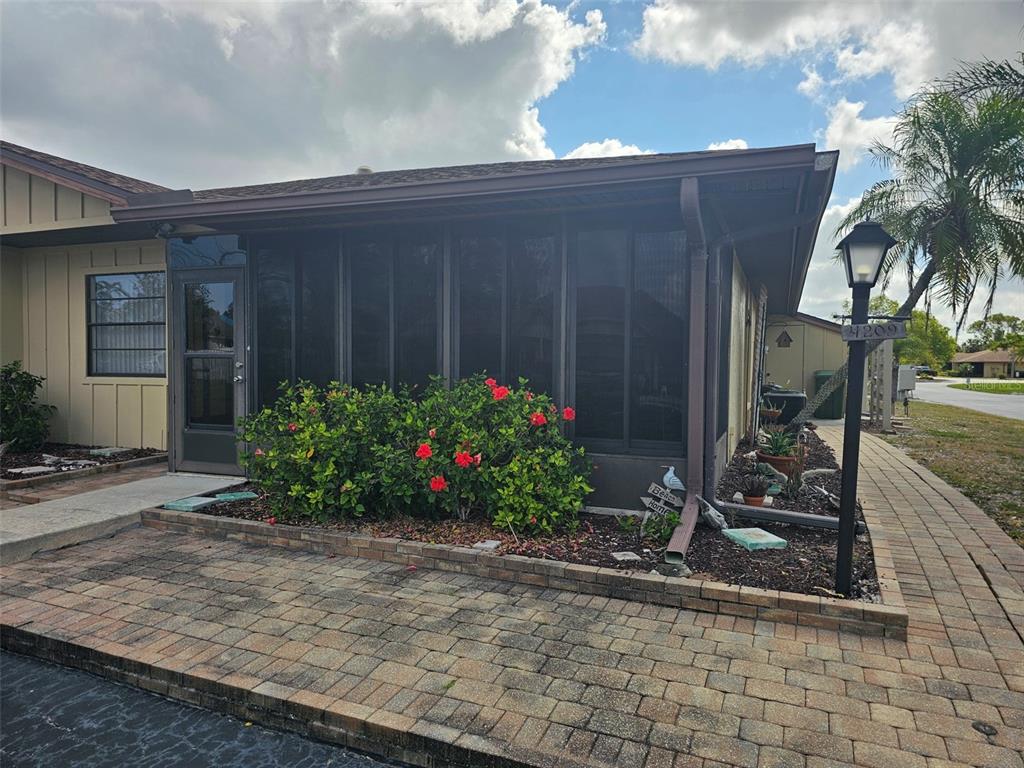 A tan house exterior features a screened-in porch, a brick paver patio, and red hibiscus bushes — 4209 66TH STREET CIRCLE W, BRADENTON, FL