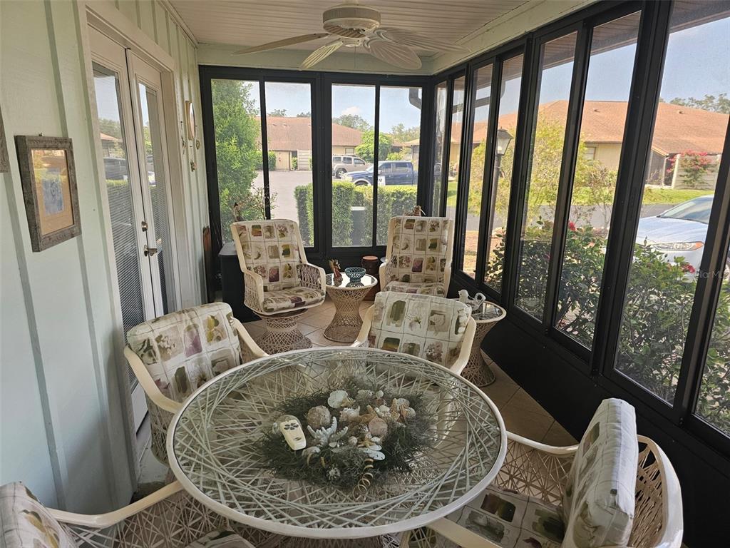 A sunroom features a glass-topped table, wicker chairs, and large windows overlooking a parking area — 4209 66TH STREET CIRCLE W, BRADENTON, FL