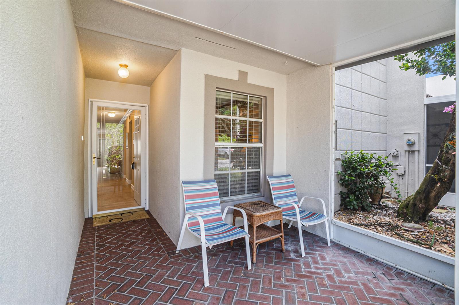 A covered brick patio features two striped chairs, a small table, and a glass door — 18900 Stewart Circle # 7, Boca Raton FL 33496, BOCA RATON, FL