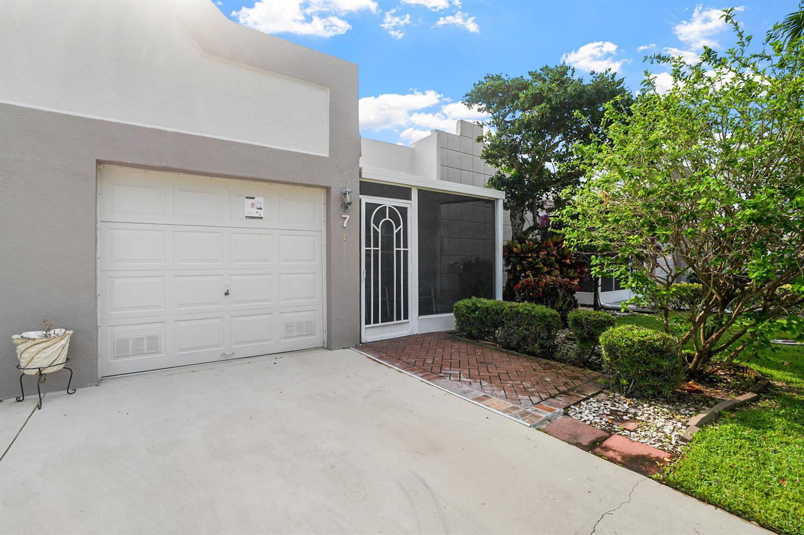 A single-story home exterior features a white garage door, a screened entryway, and landscaping — 18900 Stewart Circle # 7, Boca Raton FL 33496, BOCA RATON, FL