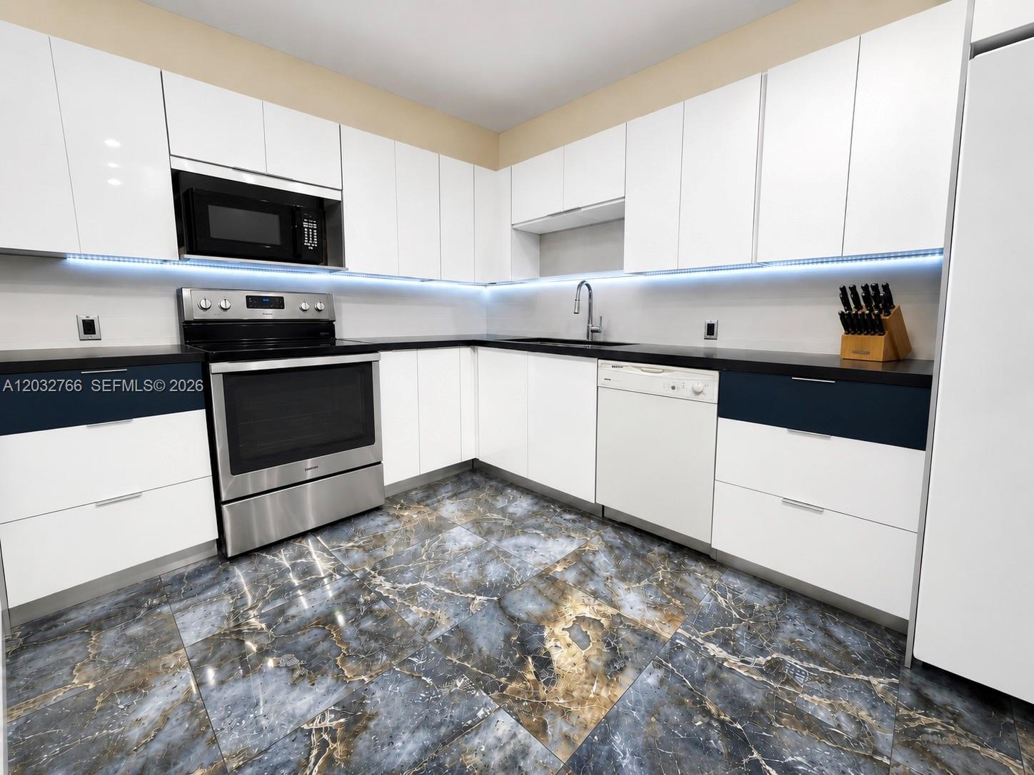 A modern kitchen features white cabinets, stainless steel appliances, black countertops, and patterned tile flooring — 4200 Hillcrest Dr # 403, Hollywood FL 33021, HOLLYWOOD, FL
