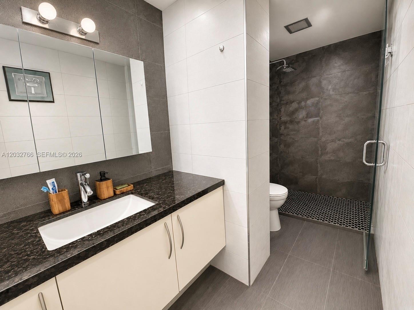 A modern bathroom features a dark granite vanity, white cabinets, and a walk-in tiled shower — 4200 Hillcrest Dr # 403, Hollywood FL 33021, HOLLYWOOD, FL