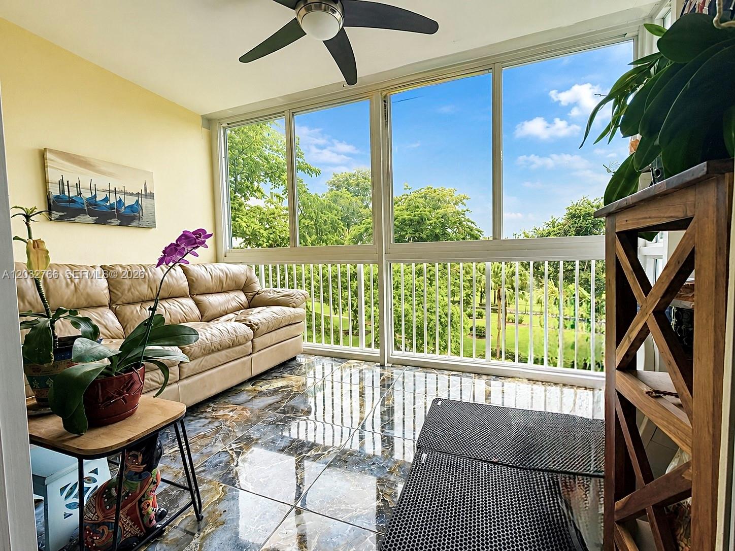 A sunroom features a tan leather sofa, marble-look tile flooring, and large windows overlooking trees — 4200 Hillcrest Dr # 403, Hollywood FL 33021, HOLLYWOOD, FL