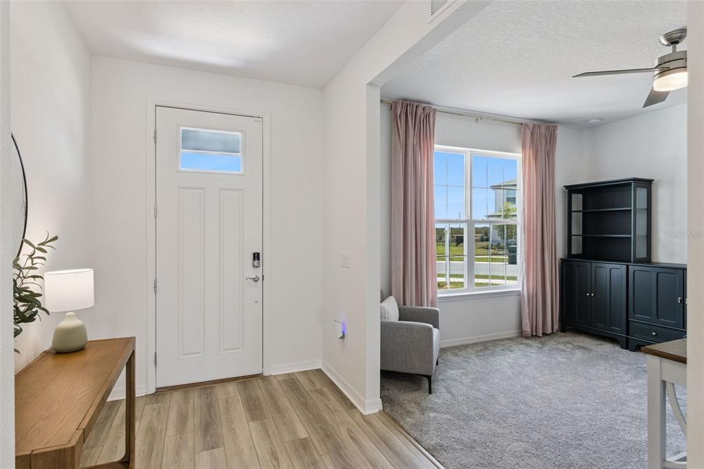 A bright entryway with wood-look flooring leads into a carpeted room with a ceiling fan — 1218 LAKERIDGE WAY, LAKE ALFRED, FL