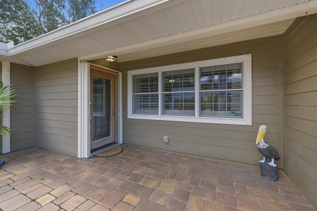 A covered entryway features a paved patio, a wooden front door, and a pelican statue — 1894 LOMA LINDA STREET, SARASOTA, FL
