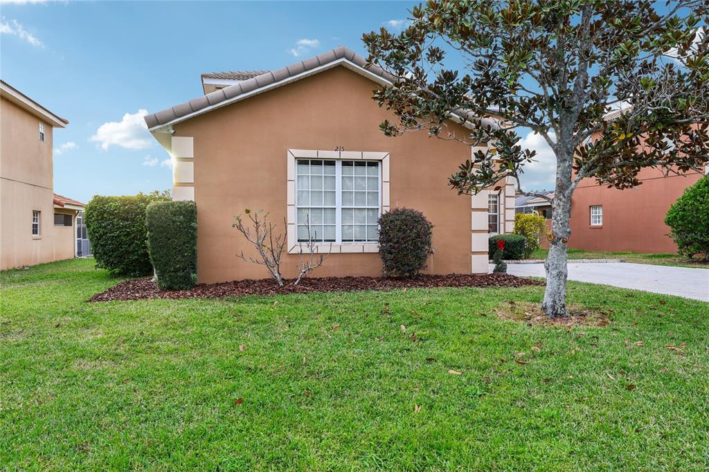 A tan single-story house with a white-trimmed window and a tree in the front yard — 215 VISTA DRIVE, DAVENPORT, FL
