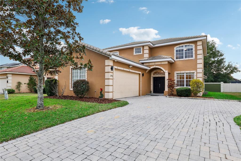 A two-story tan stucco house with a paved driveway and a two-car garage — 215 VISTA DRIVE, DAVENPORT, FL