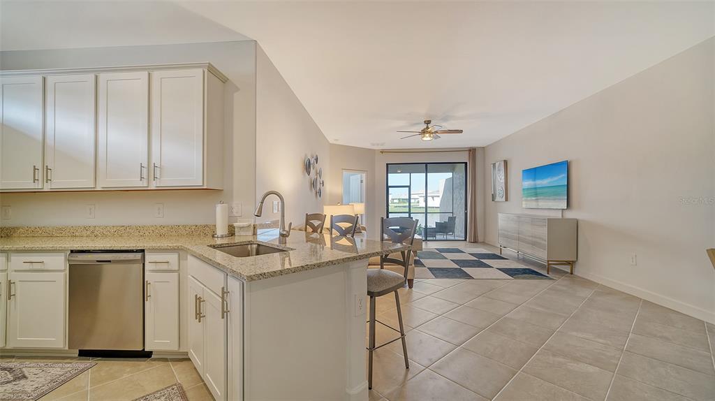 A kitchen with white cabinets and granite countertops overlooks a living area with tile floors — 15721 SUNNY DAY DRIVE, BRADENTON, FL