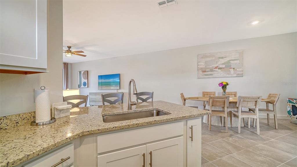 A kitchen island with a granite countertop and sink overlooks a dining area and living room — 15721 SUNNY DAY DRIVE, BRADENTON, FL