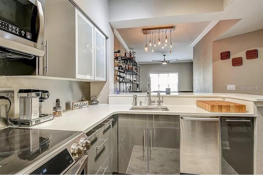 A modern kitchen features gray cabinets, white countertops, stainless steel appliances, and a pass-through window — 100 4TH AVENUE S UNIT 205, ST PETERSBURG, FL