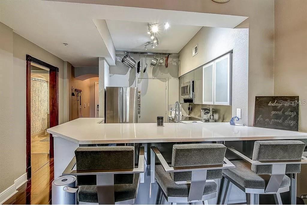 A modern kitchen features a white breakfast bar, stainless steel appliances, and hanging cookware — 100 4TH AVENUE S UNIT 205, ST PETERSBURG, FL